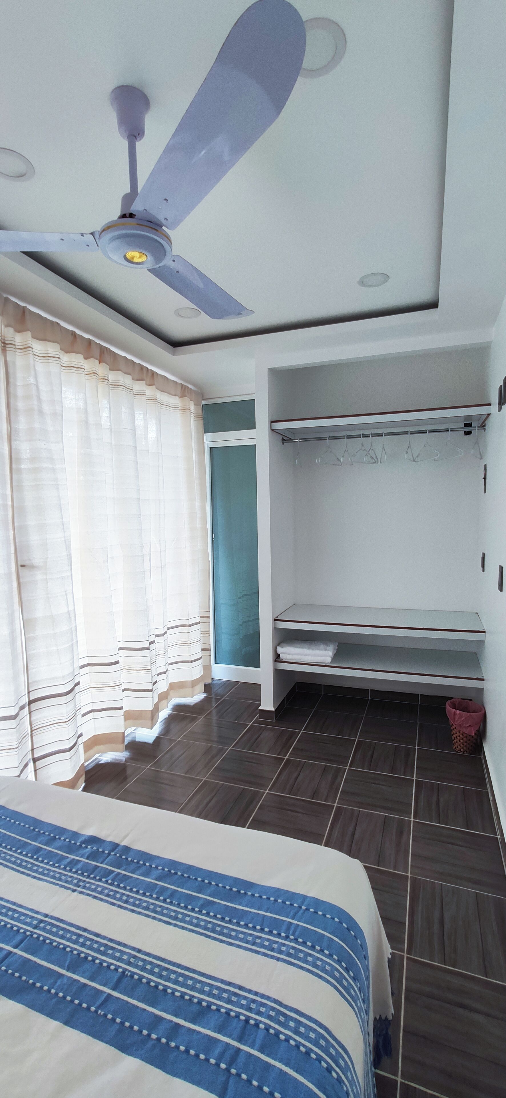 A bedroom with a bed, a ceiling fan, a wardrobe, and a window with curtains.