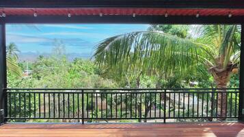 A wooden deck with a black railing, overlooking a lush garden with palm trees and other greenery.