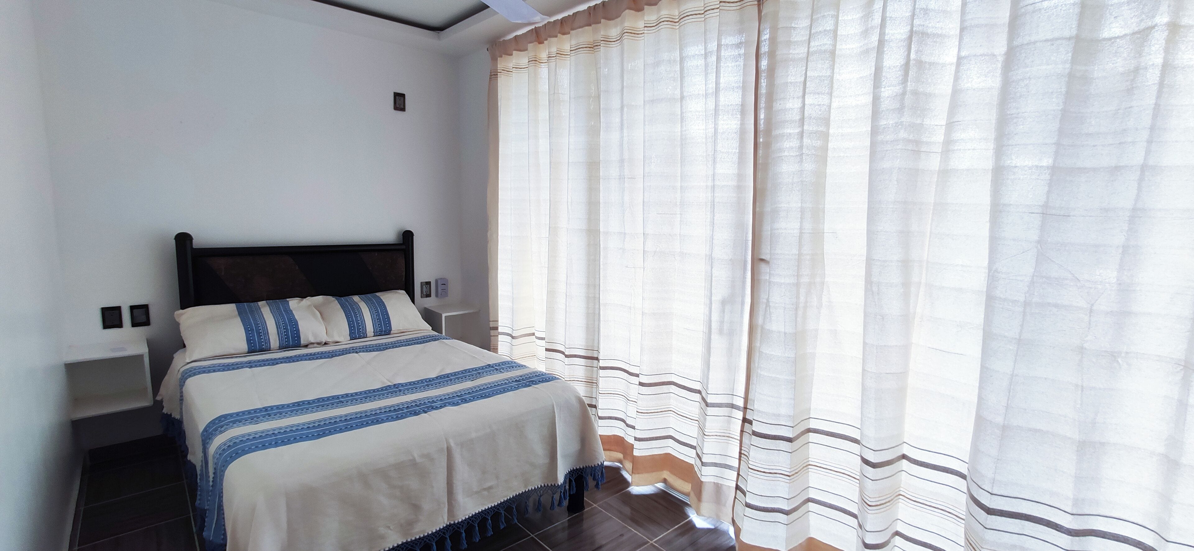 A bedroom with a bed, a nightstand, and a window with curtains.