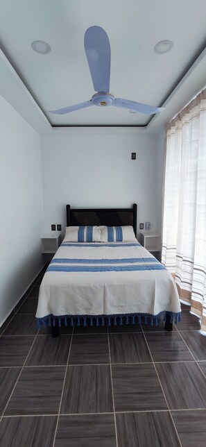 A bedroom with a bed, a ceiling fan, and a window with curtains. - Hospedaje Vida (Bajos de Chila)