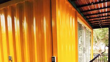 A covered wooden deck with a yellow wall, a hammock, and a metal railing.