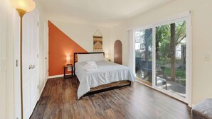 Un dormitorio con cama, mesita de noche, lámpara y vistas al exterior a través de una puerta corrediza de vidrio.