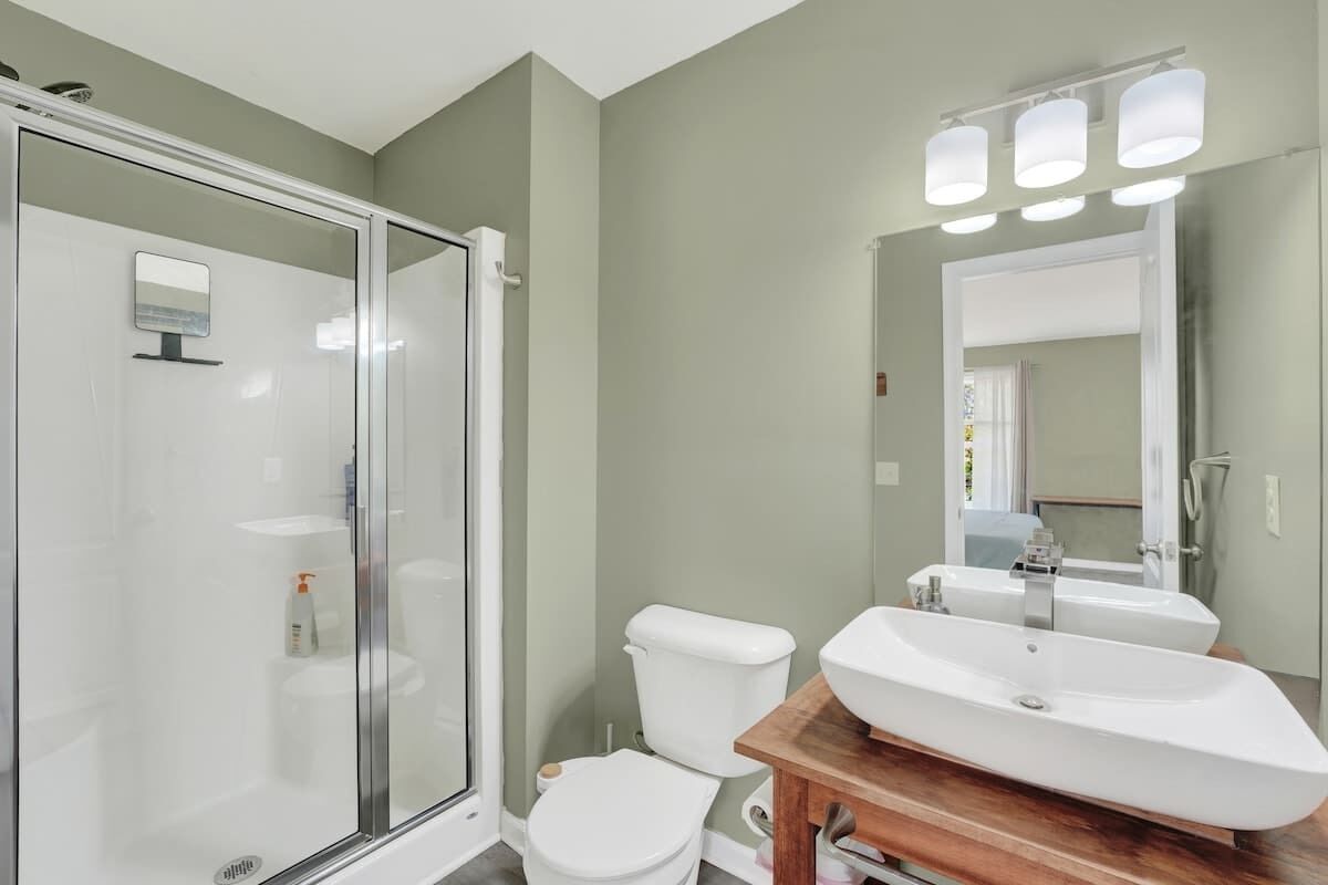 A modern bathroom with a glass shower enclosure, a white toilet, and a wooden vanity with a large sink.