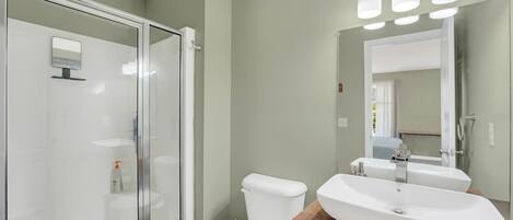 A modern bathroom with a glass shower enclosure, a white toilet, and a wooden vanity with a large sink.