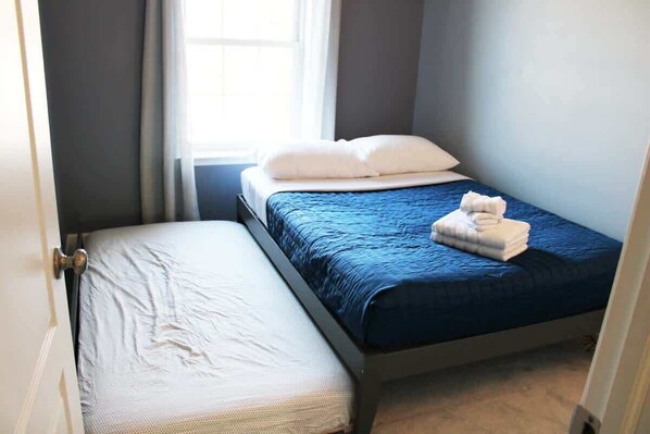A small, neatly made twin bed with a blue blanket and white pillows, a white mattress, and a folded towel on the bed. - Spacious 4BR | 4B Townhouse • Sleeps 8+ • Near Downtown Wilmington (Wilmington)