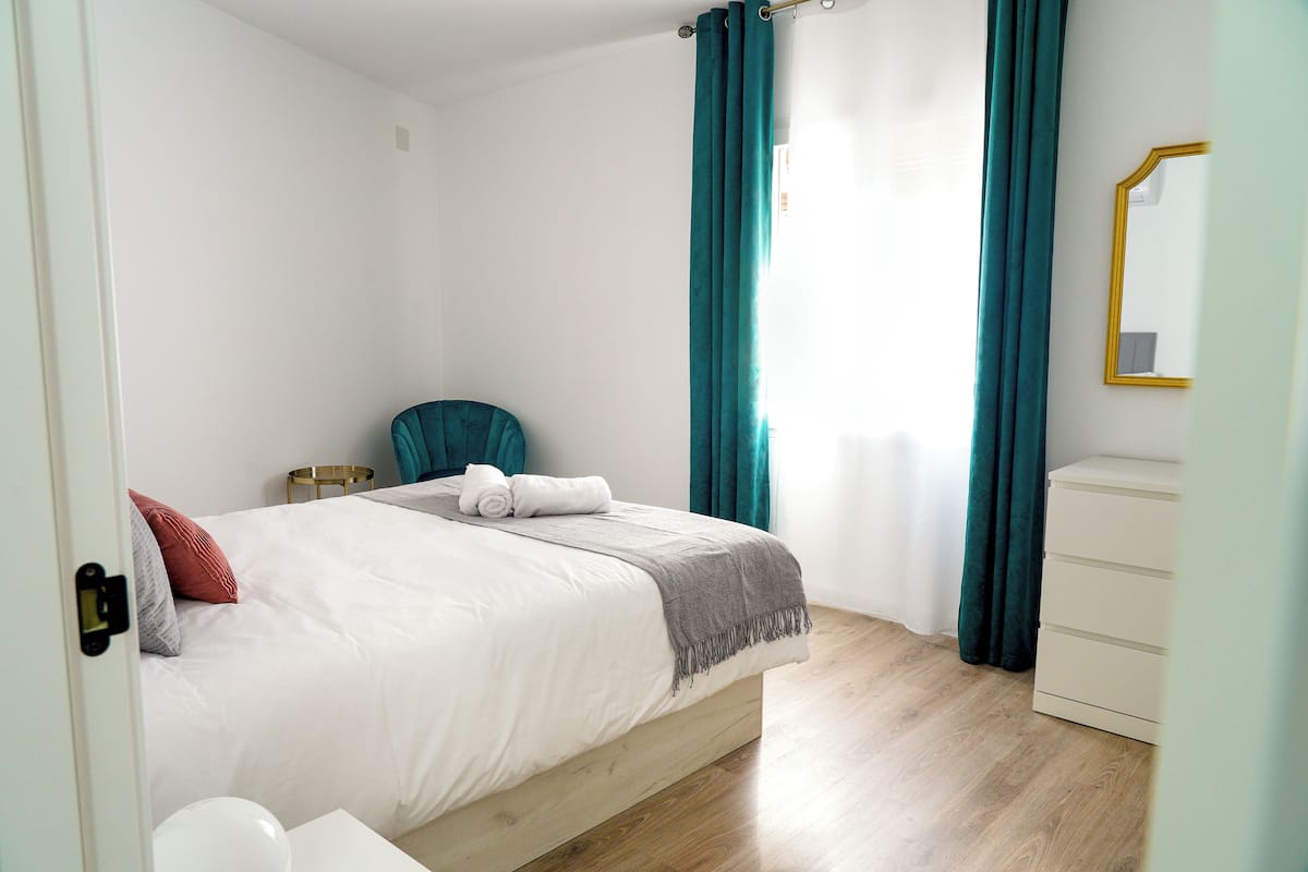 Un dormitorio con cama, una silla, cómoda y espejo.