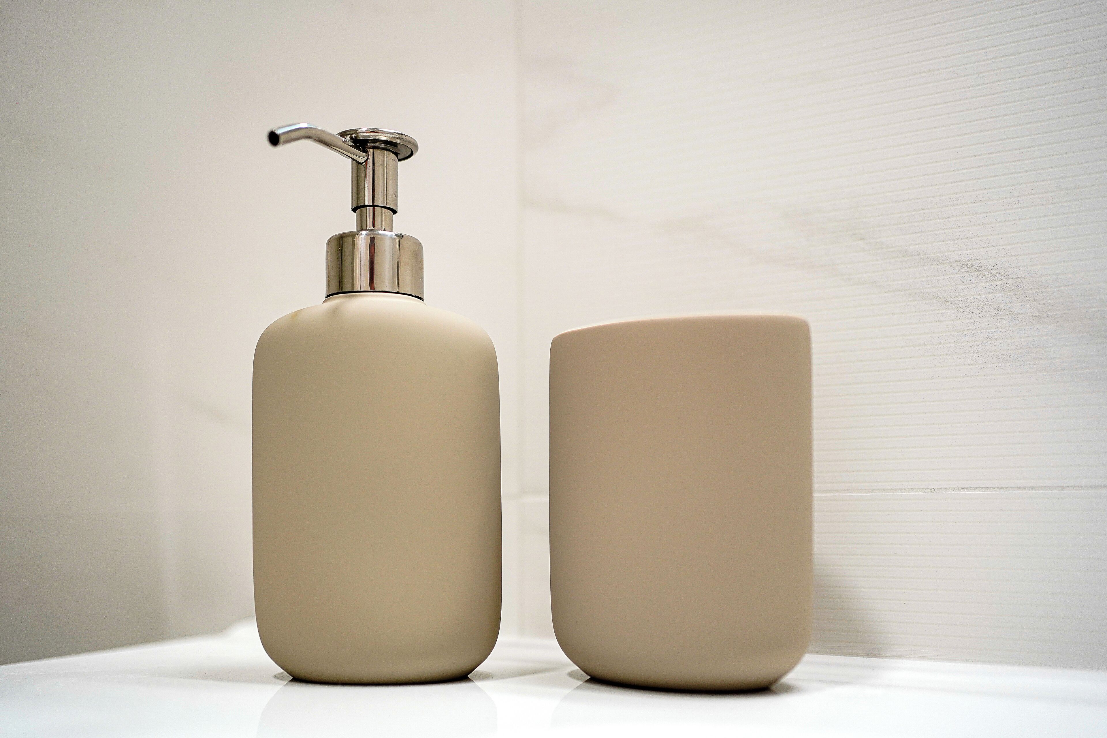 A bathroom with a white sink and a beige bottle of liquid soap and a beige cup.