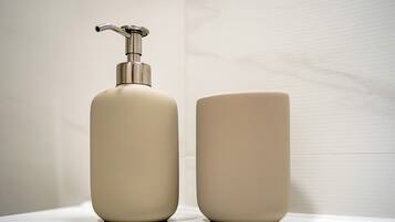 A bathroom with a white sink and a beige bottle of liquid soap and a beige cup.