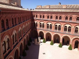Un patio central con una fuente, rodeado por edificios de ladrillo rojo con ventanas y puertas arqueadas.