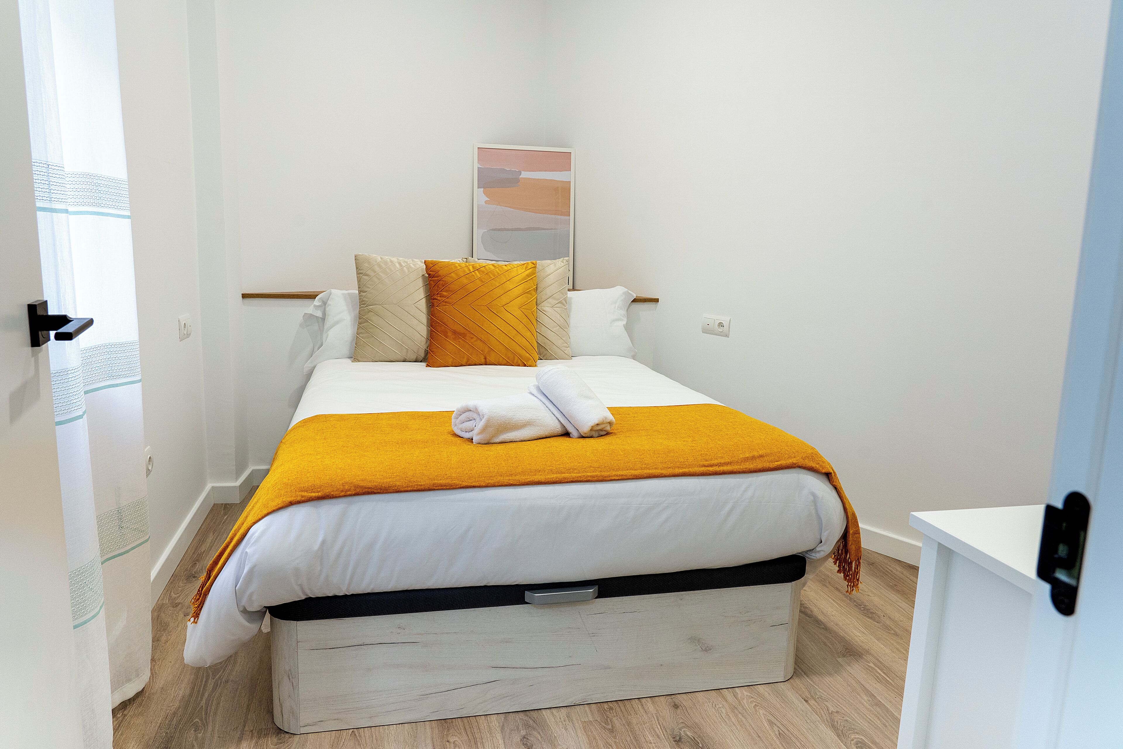 A neatly made bed with a white and yellow bedspread, a single white pillow, and a folded towel on top.