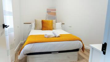 A neatly made bed with a white and yellow bedspread, a single white pillow, and a folded towel on top.