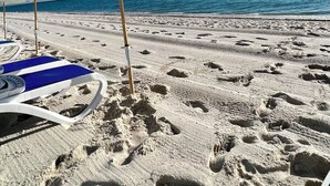 Une plage avec un parasol blanc et une chaise longue bleue.