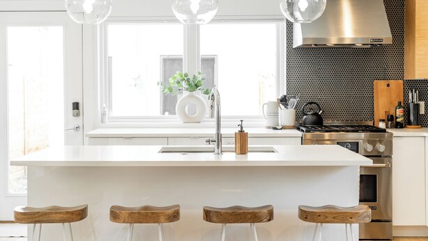 Una cucina moderna con una grande isola, luci a sospensione, una cappa aspirante in acciaio inossidabile e vista sull'esterno.