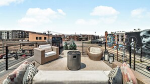 Una terrazza sul tetto con mobili in vimini, una pianta in vaso e un murale.