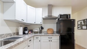 Een moderne keuken met witte kasten, een zwarte koelkast, een magnetron en een koffiezetapparaat.