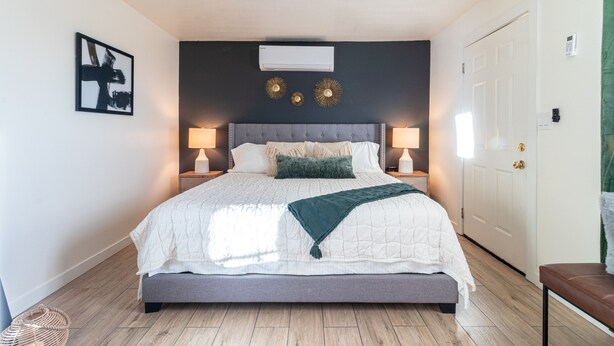 Een slaapkamer met een groot bed, twee bedlampen, een plafondventilator en een aan de muur bevestigde airconditioning.