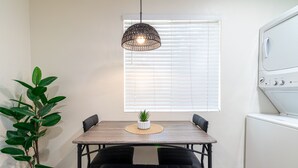 Een eetgedeelte met een houten tafel, zwarte gewatteerde banken, een geweven placemat en een hangende lamp.