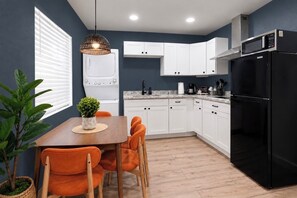 A modern kitchen with white cabinets, a black refrigerator, and a dining area with orange chairs.