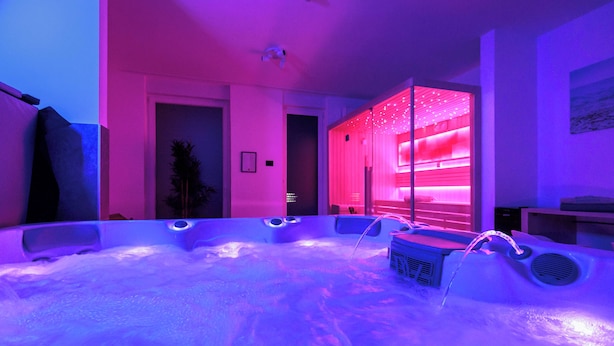A modern spa room with a hot tub, pink ambient lighting, and a view of the adjacent room. - TESLA Residence Subotica (Subotica)