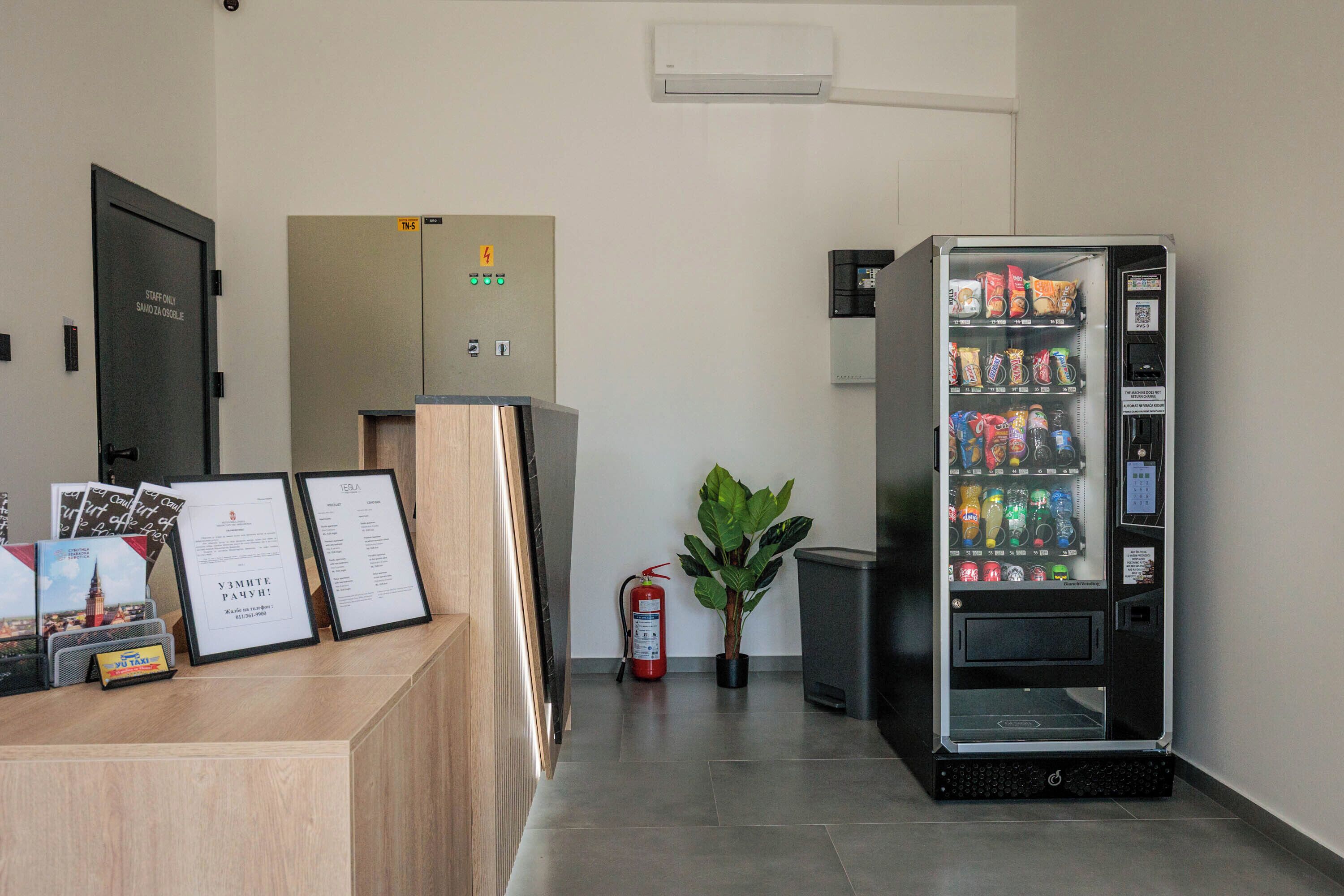 A reception area with a vending machine, a fire extinguisher, a potted plant, and a sign indicating the elevator direction.
