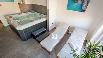 Relax in a serene space with a large hot tub, two single beds, and a calming coastal art piece.