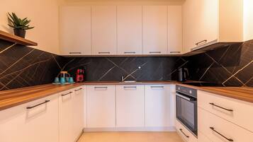 Una cocina moderna con armarios blancos, salpicadero de mármol negro y encimeras de madera.