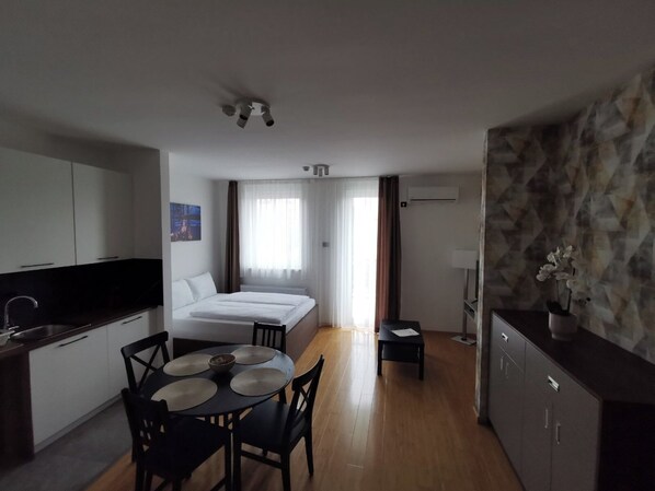 A compact hotel room with a bed, a small table with chairs, a kitchenette, and a bathroom. - TESLA Residence Subotica (Subotica)