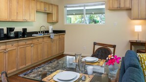 A kitchen with wooden cabinets, a dining table set with plates and cutlery, and a window with a view of greenery. - Private Updated Studio Close to Volcanoes National Park (Volcano)