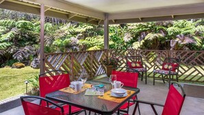 A covered outdoor seating area with red chairs and a table, surrounded by lush greenery and a decorative fence. - Private Updated Studio Close to Volcanoes National Park (Volcano)