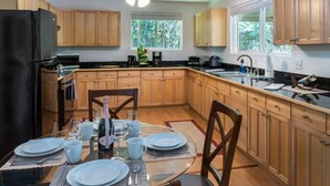 A modern kitchen with wooden cabinets, a black refrigerator, and a dining area set for four with a glass table and chairs. - Whole House Rental- Modern Two-Unit Bungalow (Volcano)