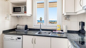 Una cocina equipada con microondas, tostadora, lavabo y lavavajillas. Hay una ventana con vistas al mar.