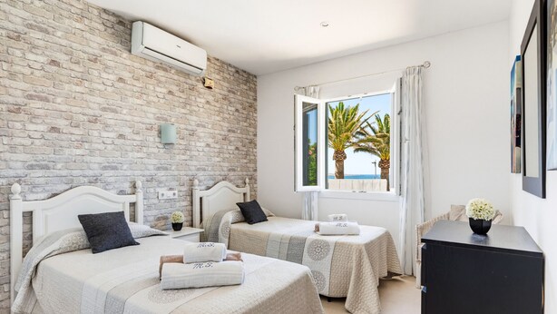 Habitación de hotel con dos camas, una pared de ladrillo, una ventana con vistas y un armario negro.