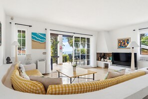 A modern living room with a sofa, a TV, and a dining area with a table and chairs.