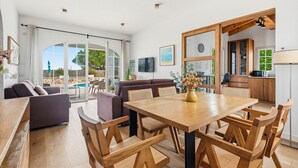 A spacious living area with a wooden dining table, sofas, and a view of the outdoor pool. - Villa Rouss by Escape Home (Calan Porter)