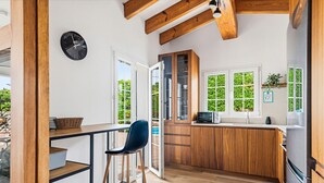 A modern kitchen with wooden cabinets, a built-in microwave, and a large window. - Villa Rouss by Escape Home (Calan Porter)