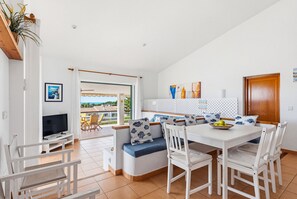 Una sala de estar moderna con televisor, zona de estar, mesa de comedor y vistas al exterior.