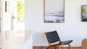 A modern interior with a white wall, a framed black and white beach scene, and a woven chair. - East 20 @ Crescent Head (Crescent Head)
