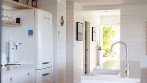A modern kitchen with white cabinetry, a built-in refrigerator, a coffee machine, and a sink with a stainless steel faucet. - East 20 @ Crescent Head (Crescent Head)
