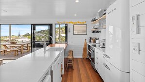 A modern kitchen with a large island, wooden stools, and a view of the outdoors. - East 20 @ Crescent Head (Crescent Head)