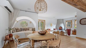 Un salón amplio con una mesa redonda de madera, asientos cómodos, una chimenea y un ventanal que proporciona luz natural.