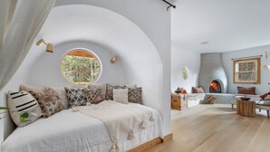 Un dormitorio acogedor con techo curvo, ventana redonda y chimenea.