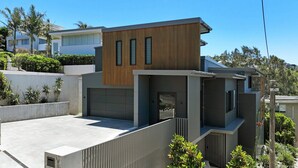 A modern two-story house with a garage, a wooden upper floor, and a concrete lower floor. - Austral House - Ultimate Coastal Retreat (Avoca Beach)