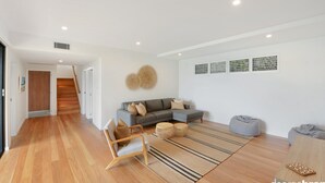 A modern living room with a grey sectional sofa, a wooden chair, a grey bean bag, and a striped rug. - Austral House - Ultimate Coastal Retreat (Avoca Beach)