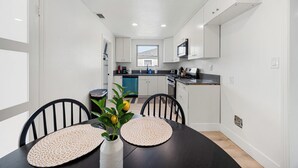 A modern kitchen with white cabinets, a black countertop, and a dining area with a black table and chairs. - Dapper 2-Bedroom Abode: Chic & Cozy (Sacramento)