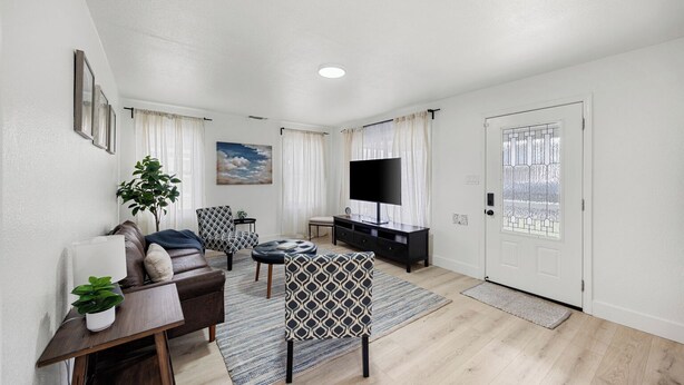 A modern living room with a sofa, armchair, TV, and a door with a glass panel. - Dapper 2-Bedroom Abode: Chic & Cozy (Sacramento)
