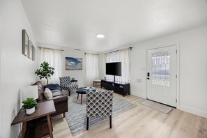 Un salon moderne comprenant un canapé, un fauteuil, un téléviseur et une porte dotée d’un panneau de verre.