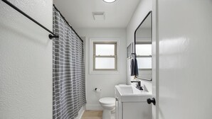 A bathroom with a shower, toilet, and sink. - Dapper 2-Bedroom Abode: Chic & Cozy (Sacramento)