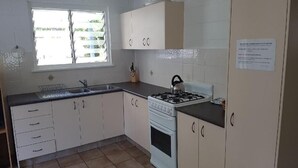 Une cuisine avec des meubles blancs, une cuisinière à gaz et une fenêtre avec des stores.