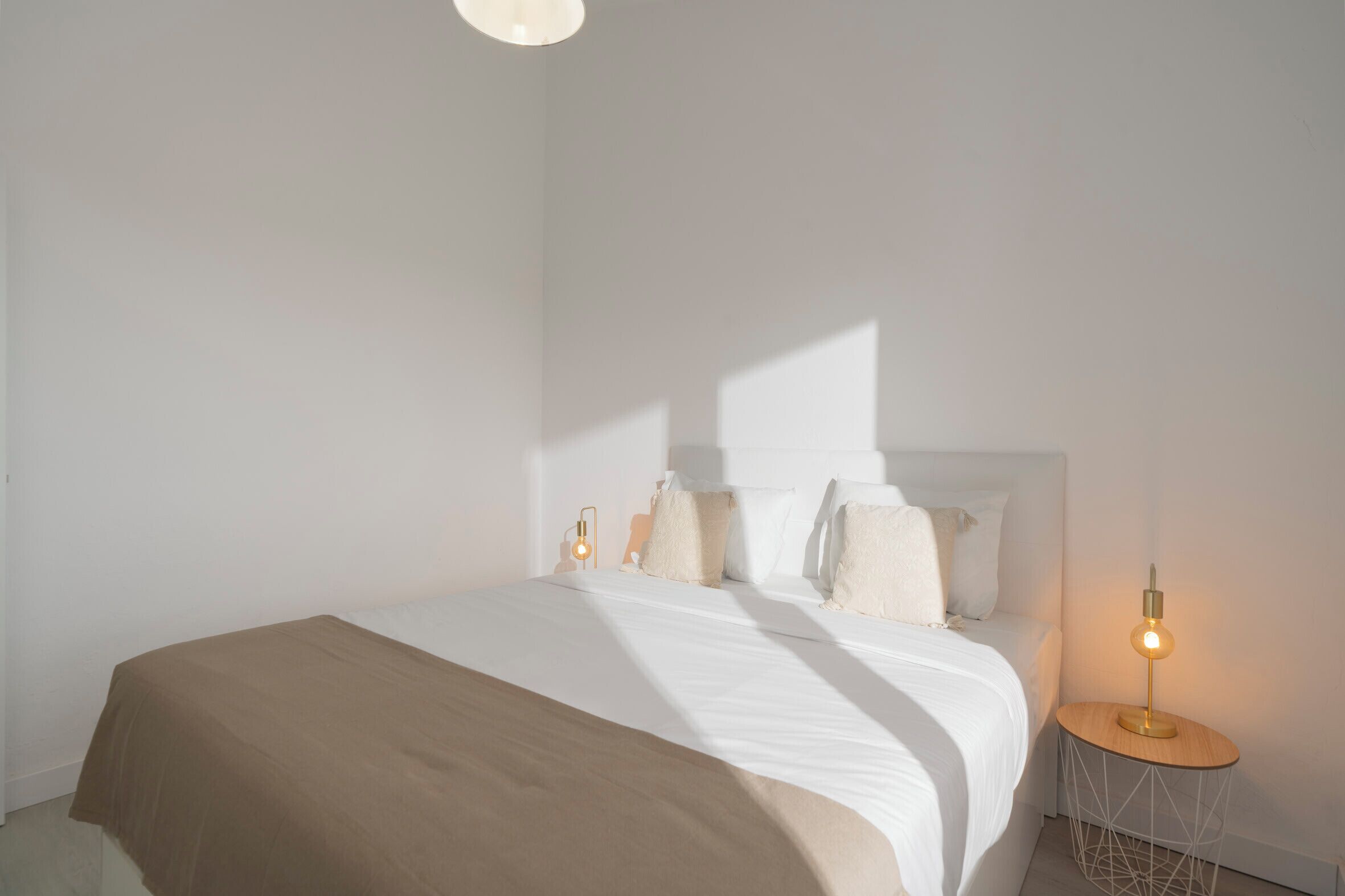 A minimalist bedroom with a bed, bedside lamps, and a plain wall.