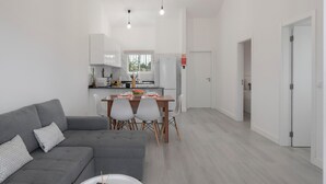 Un salon moderne avec un canapé gris, une table à manger et des chaises, et une cuisine en arrière-plan.